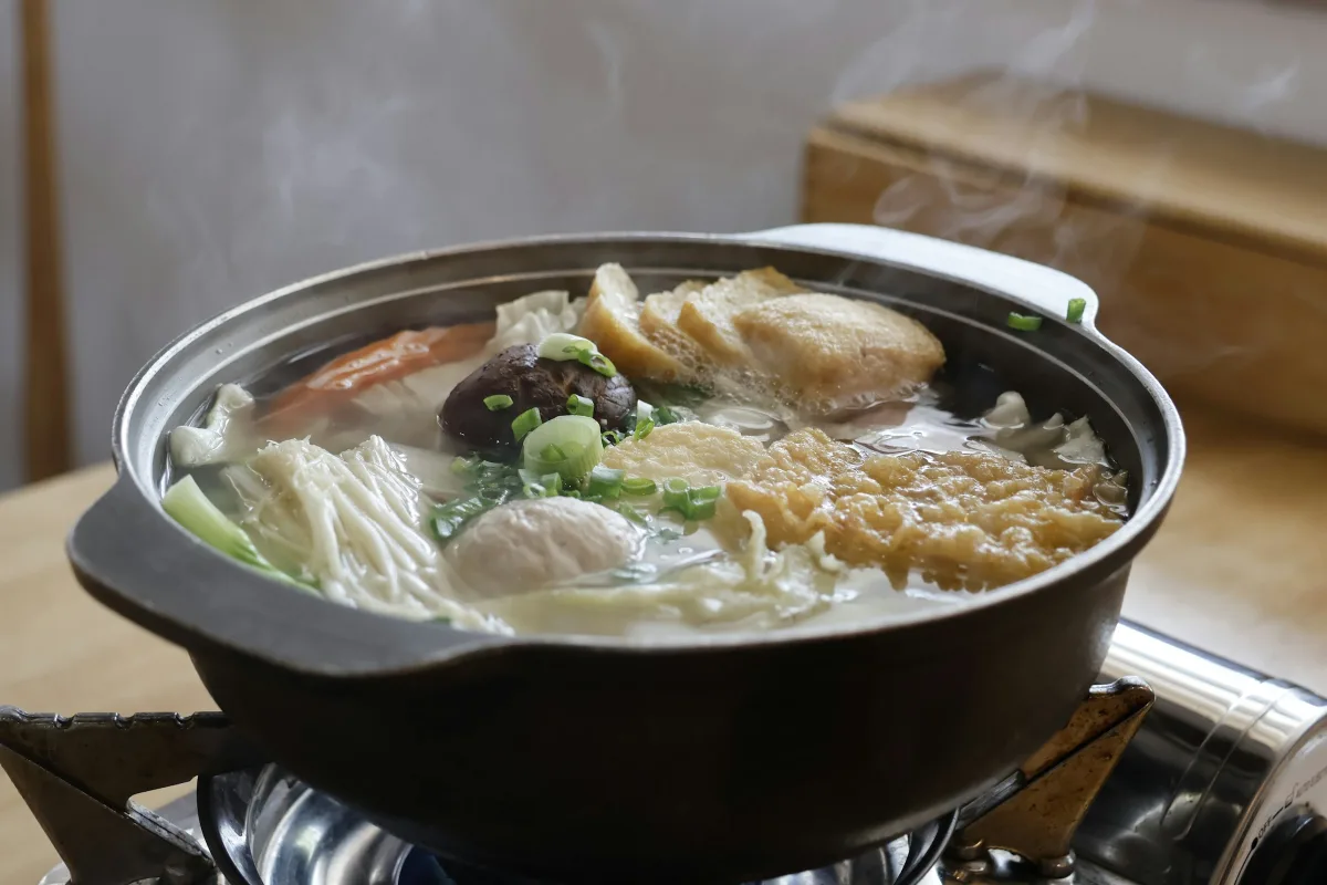 Nồi lẩu bốc khói trên bàn gỗ, đĩa rau xanh bên cạnh